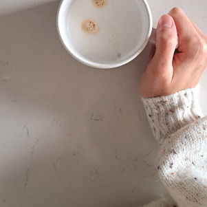 kobieca dłoń w swetrze trzyma kubek z kawą na marmurowym blacie