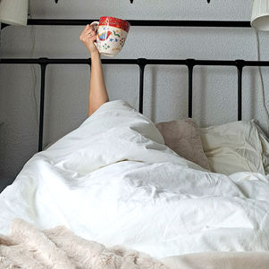 kobieca ręka trzymająca kubek i wystająca z białej pościeli 