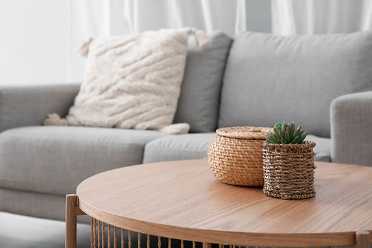 Wooden coffee table with with houseplant and wicker basket near grey sofa in living room.j