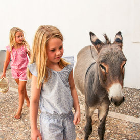 Two girls wearing a jumpsuit walking next to a donkey