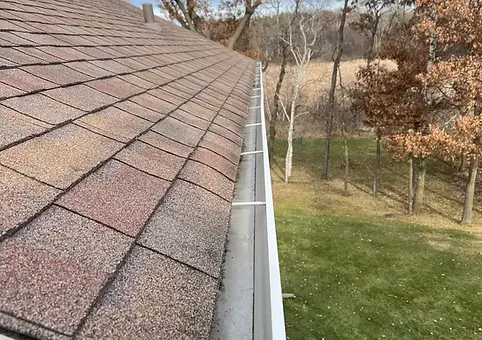 A clean, empty white gutter along a shingled roof after gutter cleaning