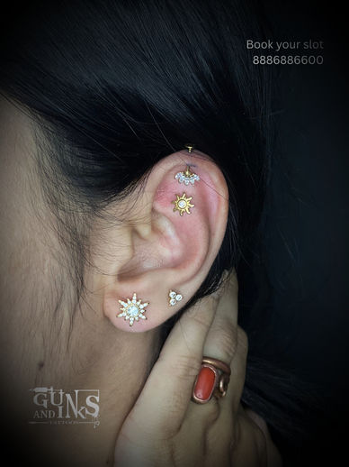 Ear with a gold cartilage piercing and two lobe piercings styled with different jewellery at Guns and Inks in Hyderabad.