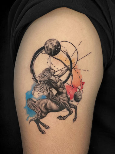 Sagittarius zodiac tattoo with centaur archer, planets and colour splash details on the upper arm at Guns and Inks in Hyderabad.