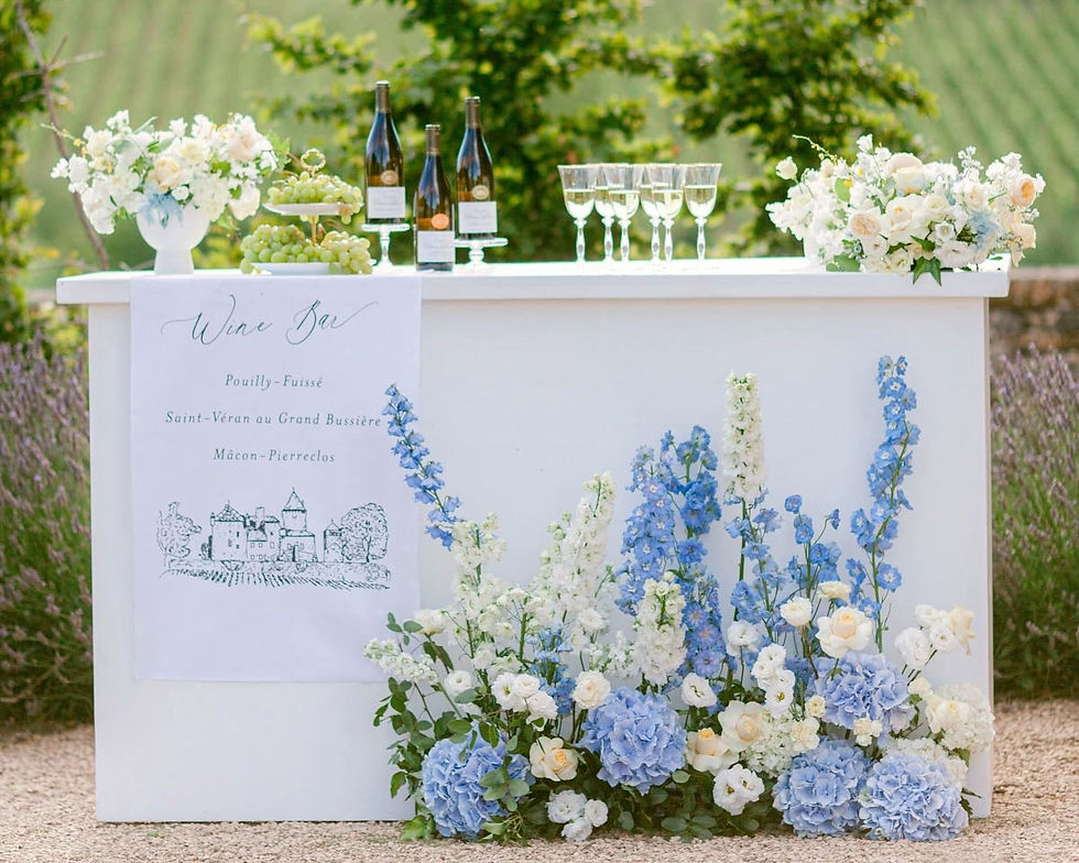 White wine bar with fresh blue and white flowers. Lush green vineyard in the background.