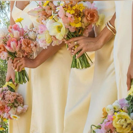Bridesmaids in soft yellow satin gowns with bright coloured bouquets