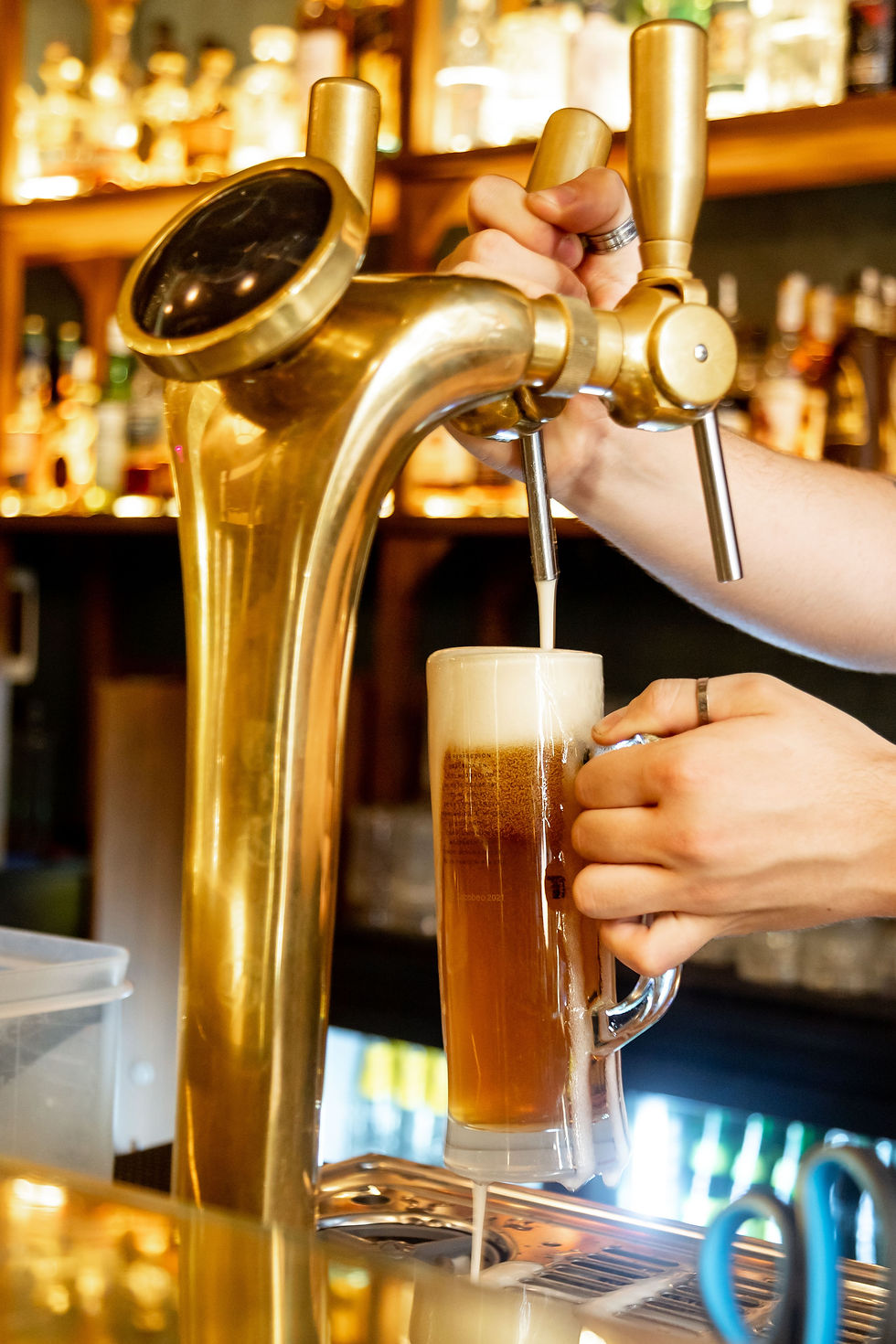 Beer pouring from a brass tap into a glass at a bar.