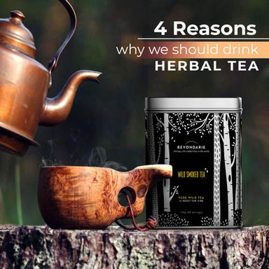 A rustic wooden cup being filled with steaming tea from a copper kettle next to a tin of wild smoked herbal tea.