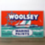 Orange and teal Woolsey Marine Paints porcelain sign with ship's wheel logo, sailboats, and Serving at Sea Since 1853