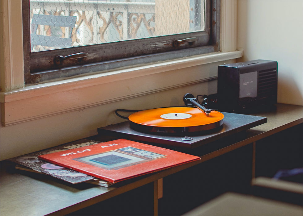 Vintage record player sitting in window. An orange record is on the retro record player with a collection of other records.