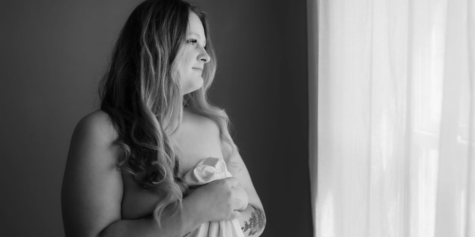 white bedsheet / boudoir pose standing by window wrapped in a white sheet during knoxville boudoir photo session / knoxville plus size bridal boudoir photography / photo by knoxville boudoir photographer rosewood boudoir / see more at rosewoodboudoir.com