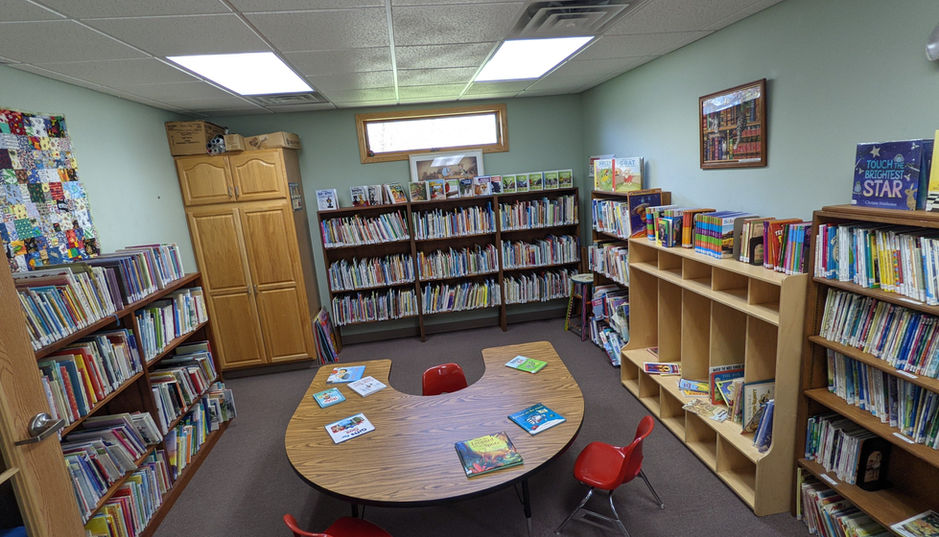 Library room with bookshelves, U-shaped table, and red chairs.