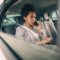 Older-Female-Executive-Works-On-Her-Computer-While-A-Driver-From-A-Non-Emergency-Medical-Transport-Car-Service-Takes-Her-To-Her-Eye-Surgery-Consultation-Appointment-In-Upstate-South-Carolina