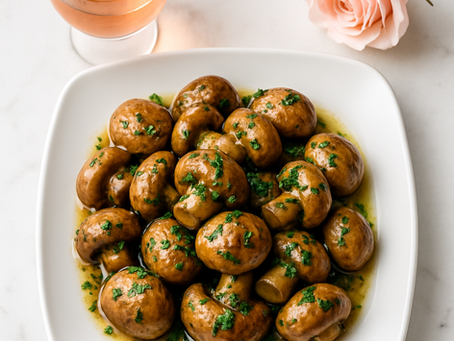 Overhead view of garlic herb roasted mushrooms on a white square plate, with a glass of wine and a pink rose on a clean white background.
