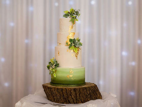 A luxury gluten free wedding cake in green with 24ct gold sat on a wooden log