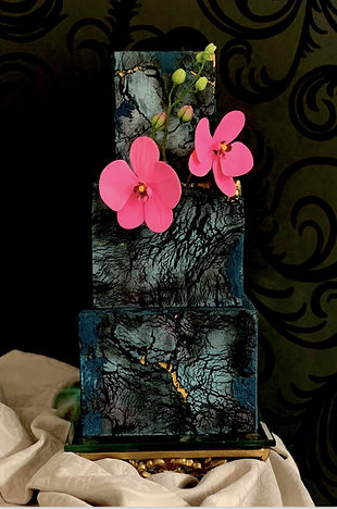 Three‑tier navy gluten‑free wedding cake with rough crown texture and silver leaf, displayed on a wooden pedestal.