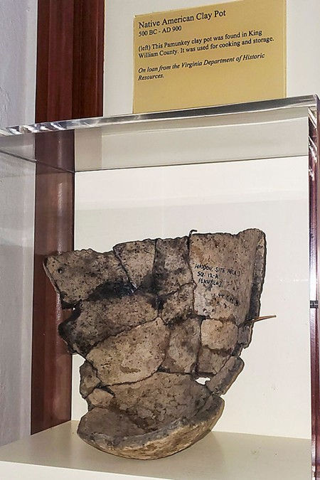 Ancient Native American clay pot displayed in a wooden-framed glass case. Notable label above describes its historical context.