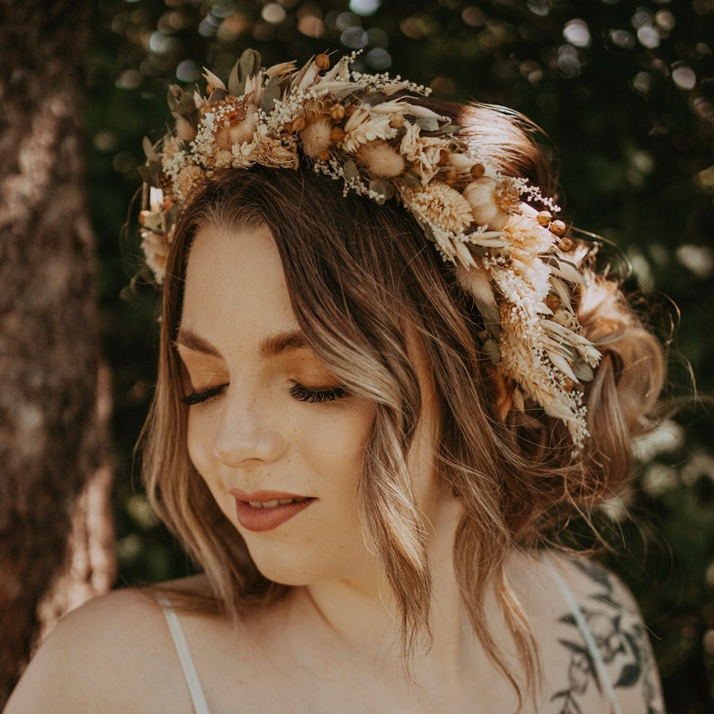 woman wearing a boho floral crown that features pampas grass, brown and orange flowers. Woman is looking down away from the camera as she smiles