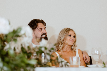 bride and groom sitting at their head reception table as they look off to the side while speeches are being given on their behalf. all via unmeasured events