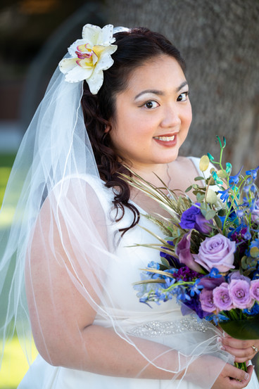 bride in her wedding day attire smiling and holding a colorful bouquet. with a floral veil. all via unmeasured events