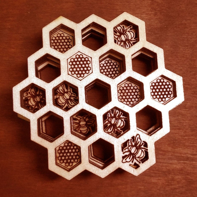 wooden honeycomb coasters held in a large honeycomb wooden display case. Photo is enlarged to show detail. Some wooden coasters are designed like bees. All sit on a dark cherry wood table. featured on the Unmeasured Events Blog