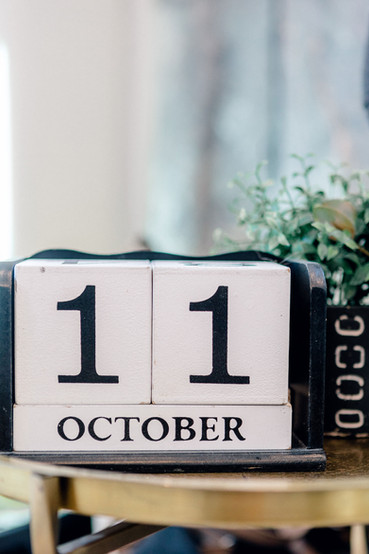 two white wooden blocks with the number 1, on a black holder that reads "October". Greenery can be seen in the background. All via Unmeasured Events