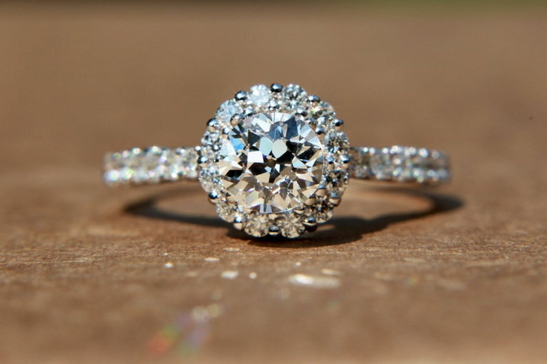 photo of a circular, vintage old European style diamond ring with a large diamond in the middle, a circular ring of diamonds around it, and a pave band. Diamond is front facing the camera