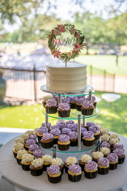 various cupcakes in shades of purple and white, with a white cake on top.all via unmeasured events
