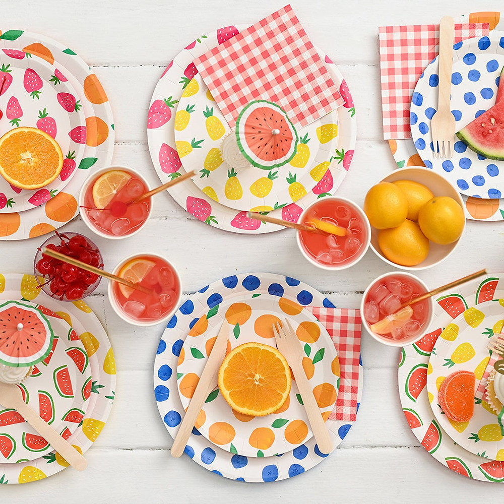 Brightly arranged paper plates in all kinds of various fruit patterns with pieces of fruit and bright drinks nearby. All Via Unmeasured Events