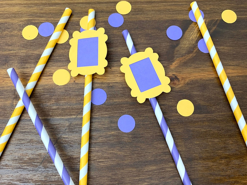 photo of purple and yellow plastic straws aligned on a wooden table with purple and yellow confetti dots sprinkled on. two of the straws have yellow and purple door frames (like Monica's apartment in friends" on them. All Via Unmeasured Events