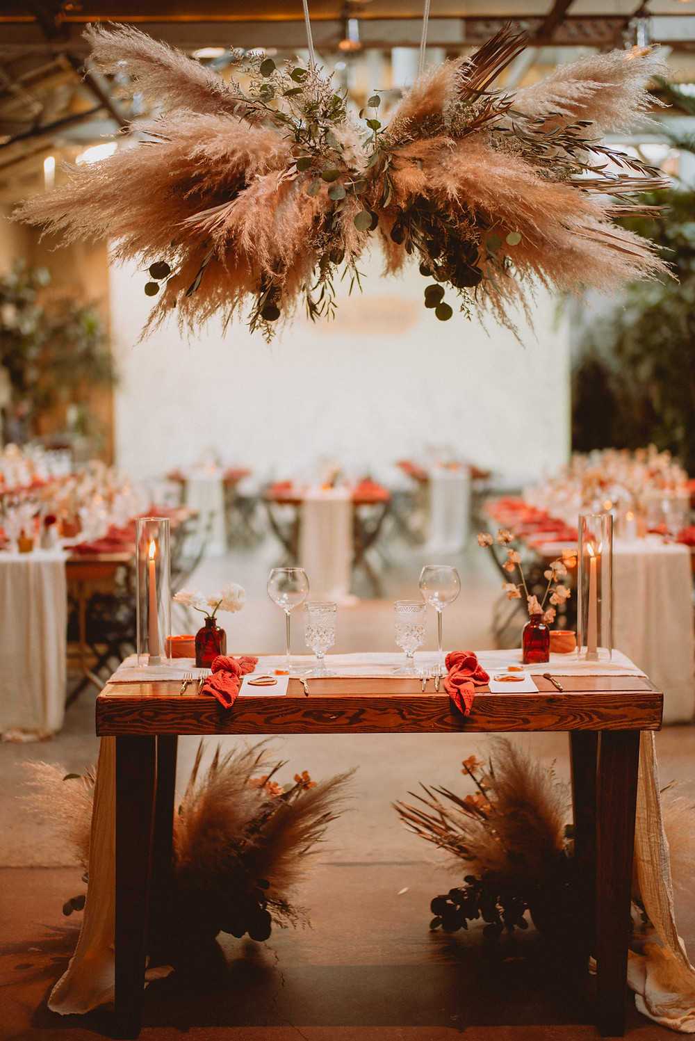Photo of a boho tablescape that shows a boho floral installation overhead. Table has decorations and place settings all over it. All via Unmeasured Events