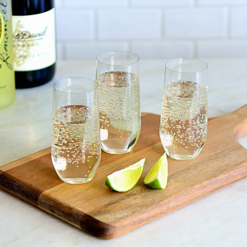champagne flutes filled with liquid on a cutting board with a few limes nearby. Bottles of liquor in the background. All via Unmeasured Events