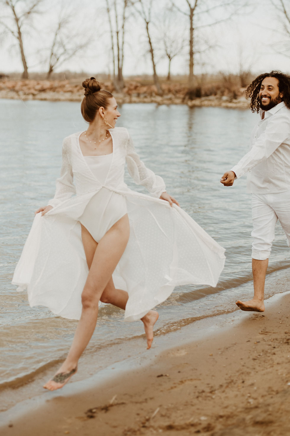 woman in a white bathing suit frolicking as she's being chased playfully by a man in an all white outfit. she is wearing a white beach coverup and smiling. All via Unmeasured events