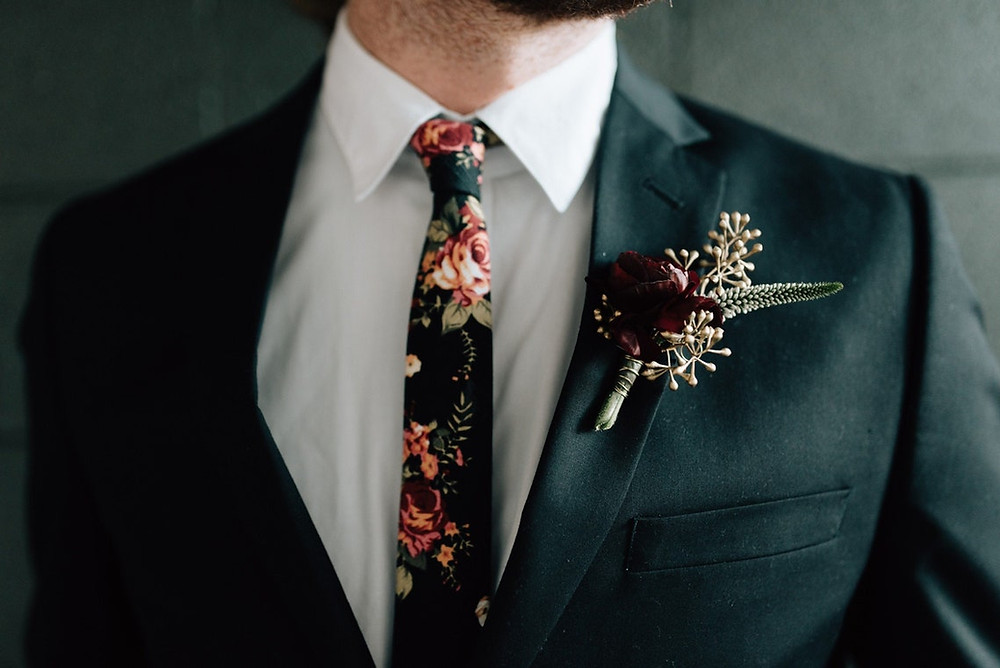 photo of a close up of a groomsmen in a dark grey suit with a dark green tie with pink florals. Mans face is slightly out of the picture. All via Unmeasured Events