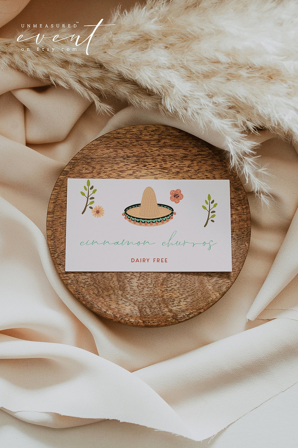 LOLITA Collection buffet card by unmeasured events. This DIY PRINTABLE food label template features colorful tequila and fiesta graphics and handwritten script font. Use these templates to edit the fonts, font color, and background color to match your event needs. card is on a small wood coaster and a piece of white fabric. all via unmeasured events
