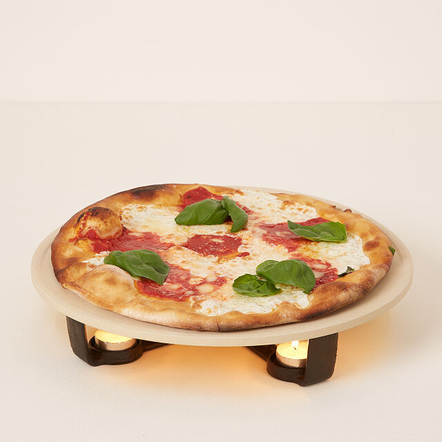 warming stone being held up on wooden stands with candles underneath that is holding a pizza