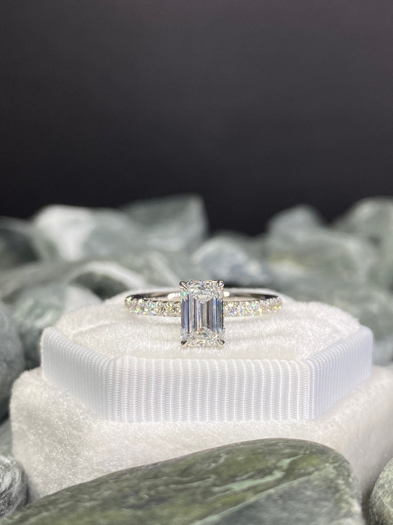 photo of a white emerald cut diamond ring front facing the camera. The ring is placed on a white cushion and is front facing the camera