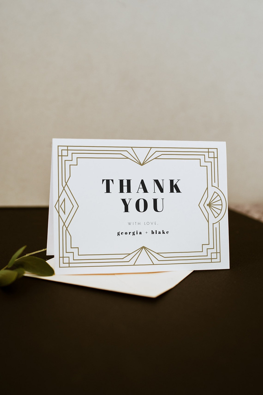 DAISY Collection Thank you card from unmeasured events that features gold Art Deco frames and styled design as well as a minimalist font. Card is on a brown table with a leaf in the background. All via Unmeasured Events