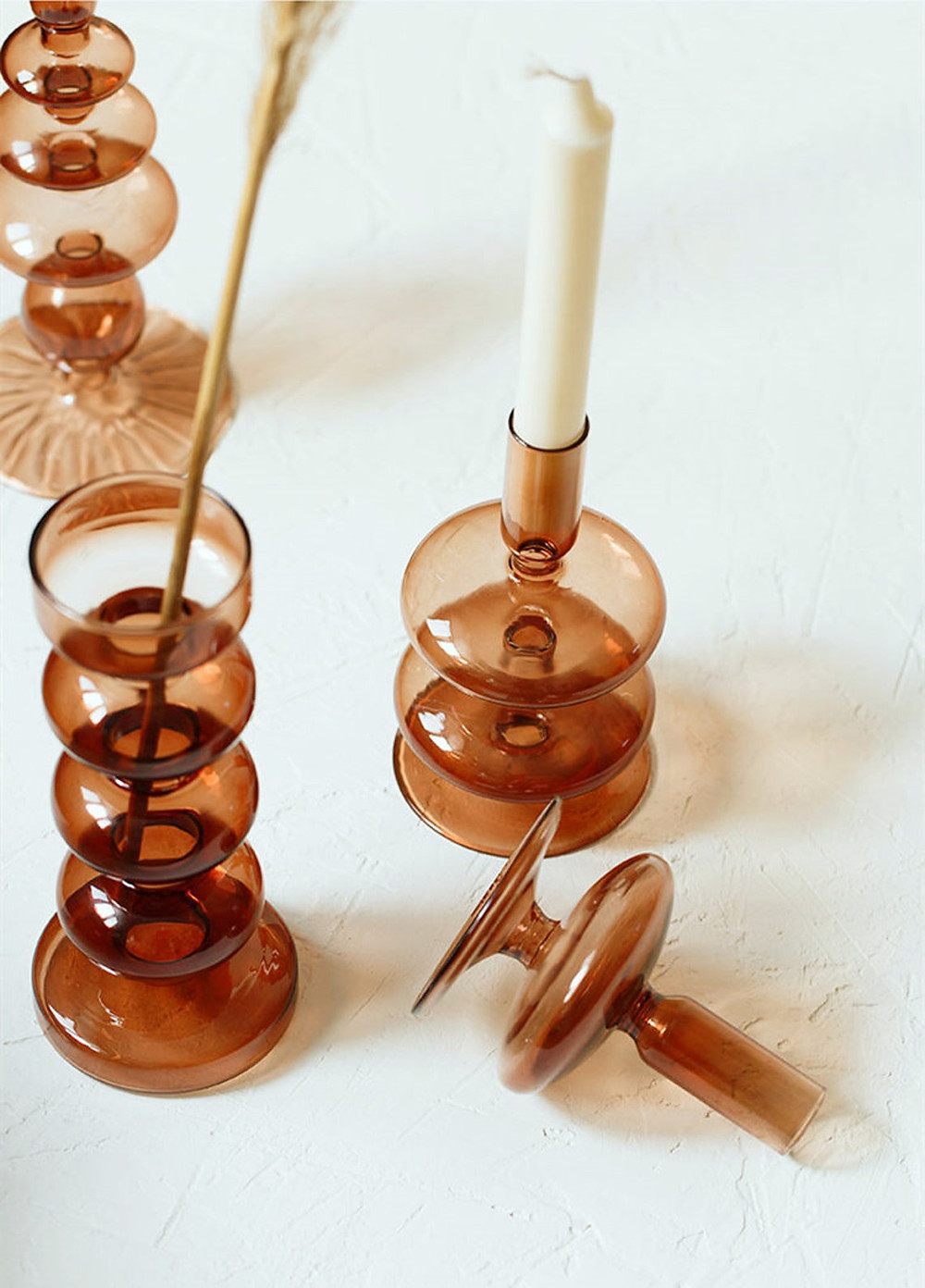 Geometric designed amber colored candle holders on a white background. There are white candlesticks or pampas grass pieces in the holders. All via Unmeasured Events