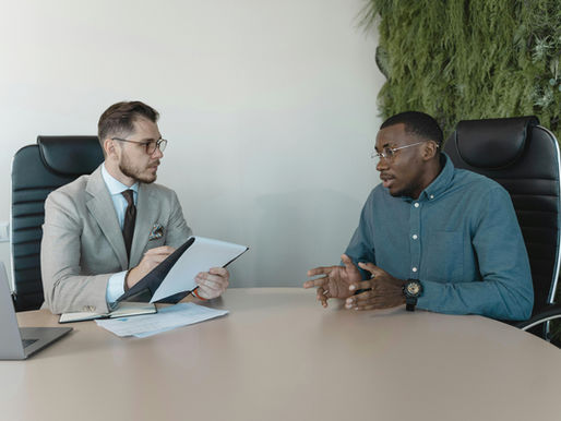 Two men in office chairs have a serious discussion at a table.