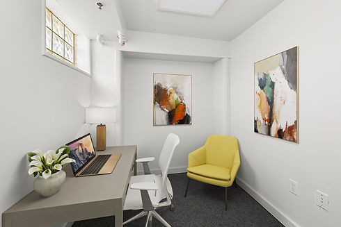 A small office with a non-opening window, private desk and chair, with a yellow side accent chair