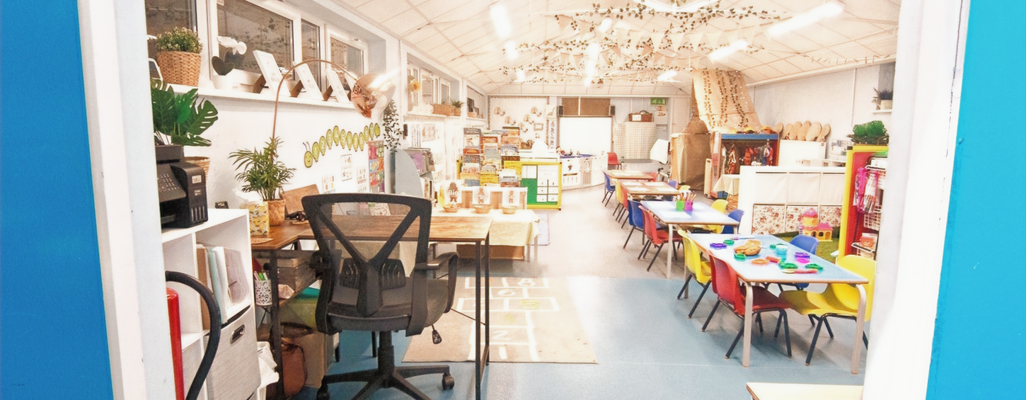 Bright classroom with tables, chairs, and toys viewed from doorway. Bright Starts Daycare.