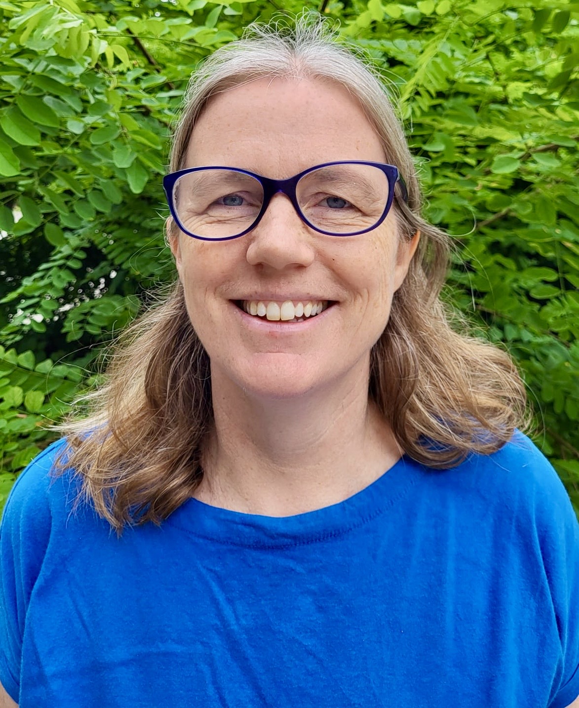 Smiling woman in glasses and blue shirt, green background.