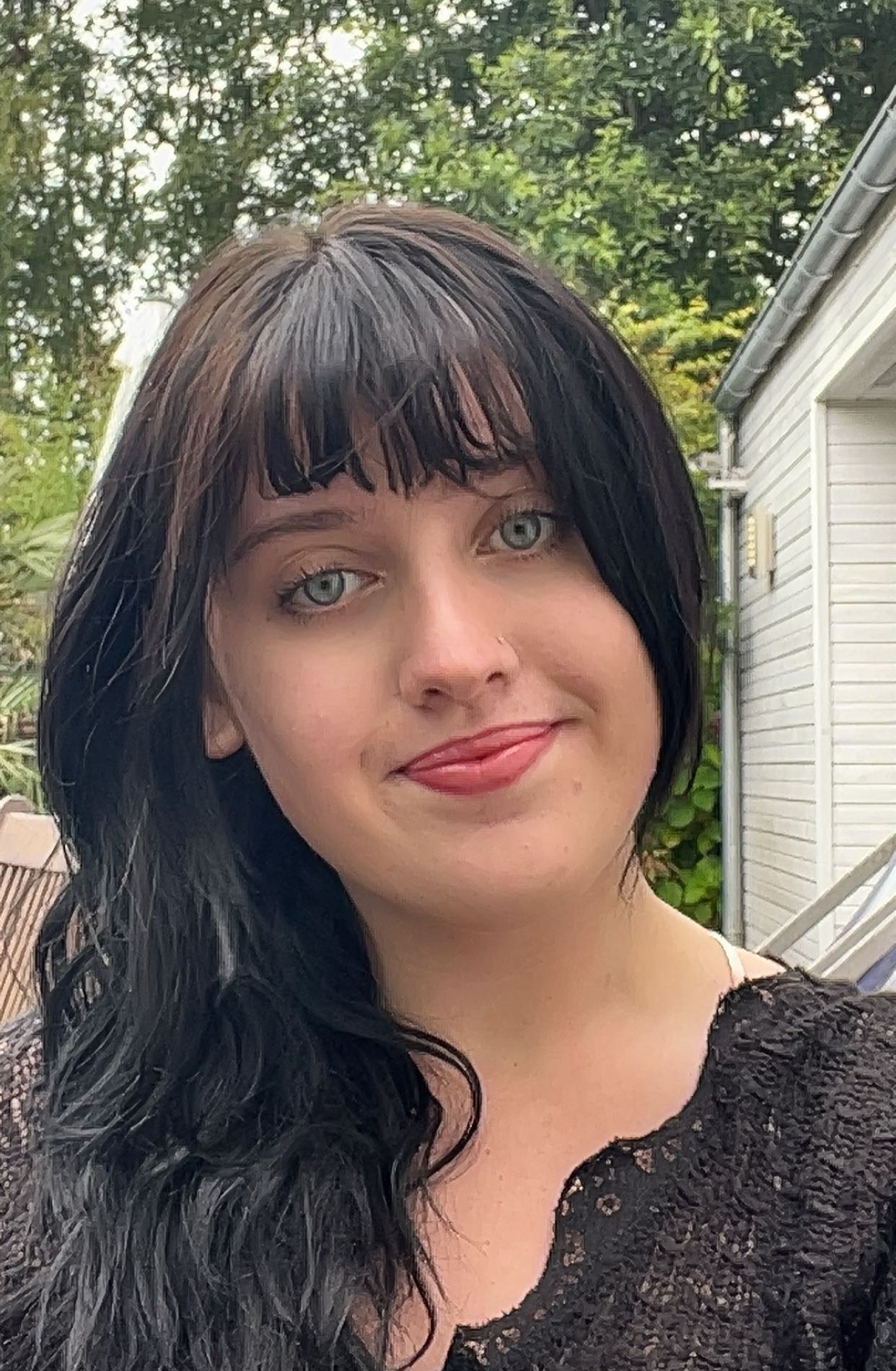 Woman with black hair smiling for the camera in front of building