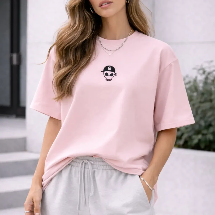 Woman standing wearing coral alien head logo t-shirt and white shorts.