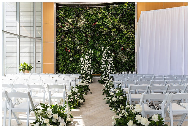 white clean wedding venue with greenery, large wedding venue seating, white backdrop, indoor wedding venue open windows and natural lighting