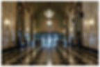 Empty ornate hotel lobby with chandeliers, marble walls, and glossy black-and-white checkered floor