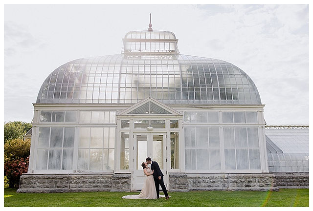 glass greenhouse as backdrop for married couple on wedding day