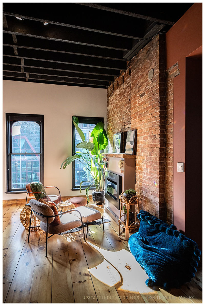 Cozy room with brick wall, sunlight through windows, modern furniture, green plant, and blue plush blanket. Warm and inviting atmosphere.