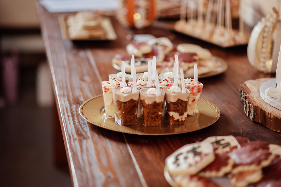 Dessert cups with spoons on a gold tray, surrounded by assorted cookies on a wooden table. Warm, inviting setting.