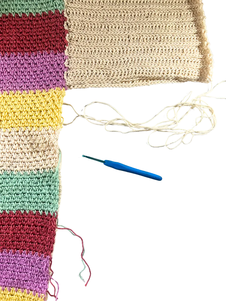 Colourful front and back crochet sweater panels laid side by side with a yarn needle and yarn tail positioned at the edge, ready to begin seaming along the side.